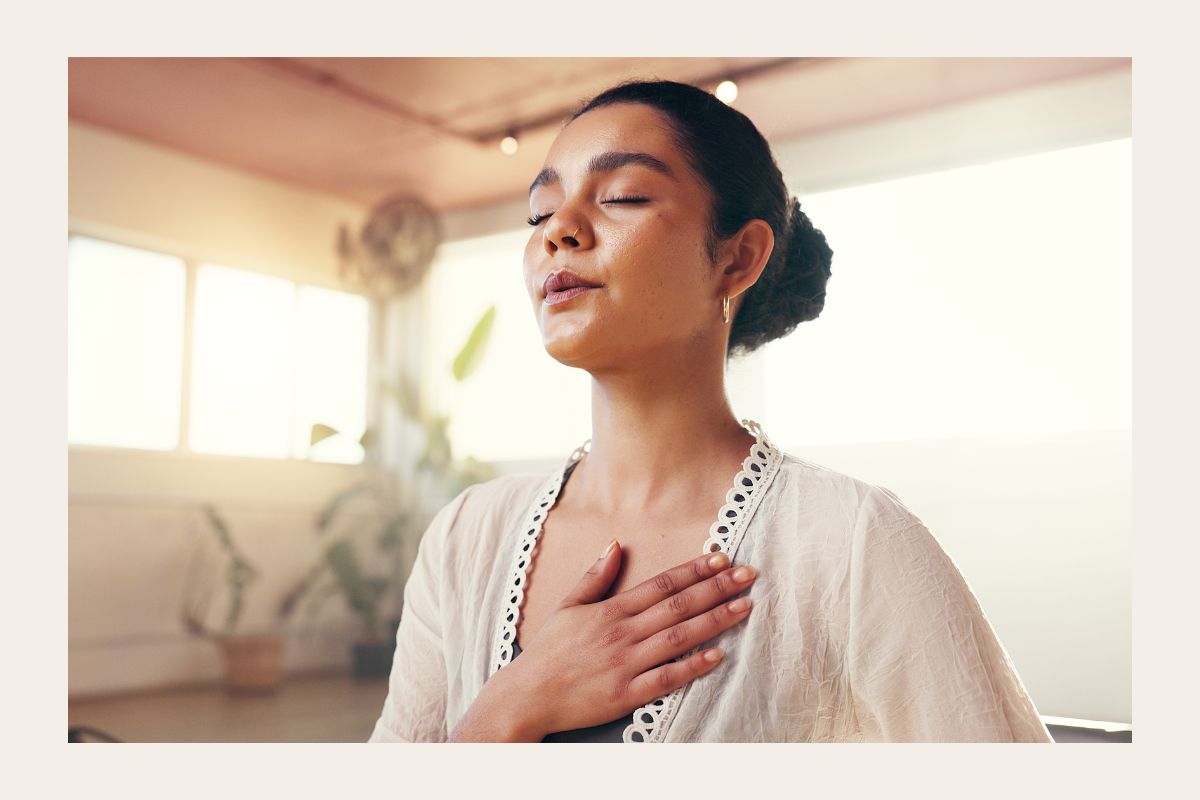 Hengitä hyvää oloa -artikkelikuva, jossa nainen hengittää rauhallisesti silmät suljettuina, käsi sydämellä, luonnonvalossa